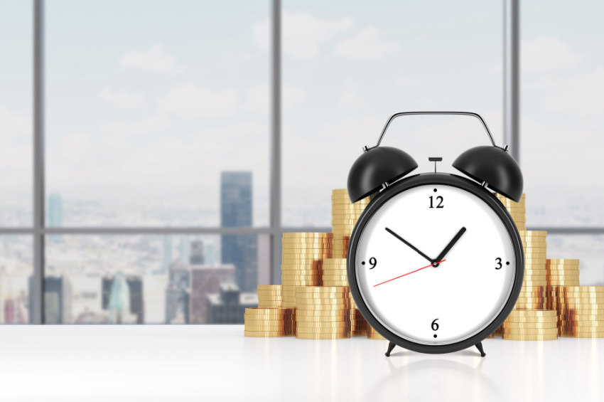 Image of an alarm clock with stacked coins in the background.