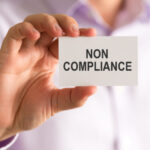 A man holds a non-compliance card in the image.