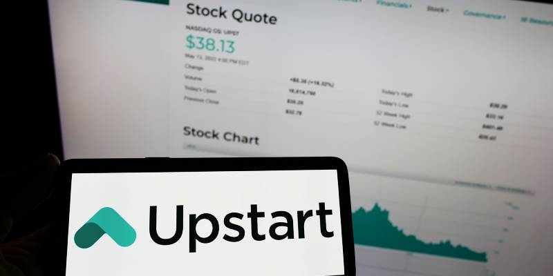 Person holding mobile phone with logo of upstart in front of a laptop screen showing upstart stock quote