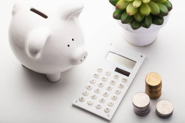 Image of a piggybank, a calculator and arranged coins kept on a table.