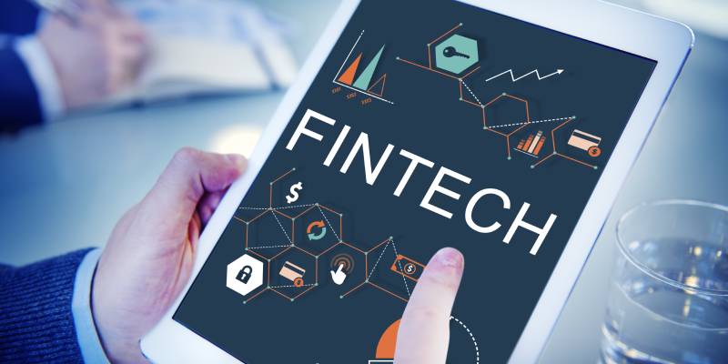 Image of a hand holding a tab and the other hand pointing at the FINTECH icon displayed on it.