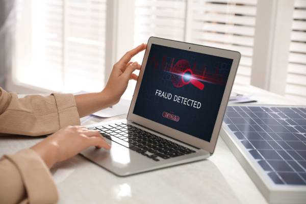Image of a woman using a laptop with the word "fraud detected" mentioned on it.
