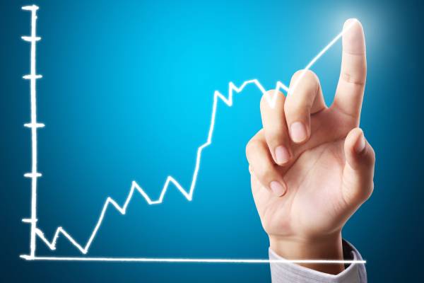 A persons hand touching a graph showing a volatile and growing trend.
