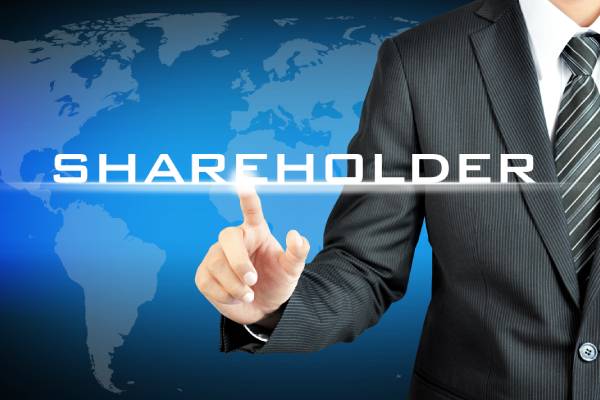 A person standing in front of a world map pointing at the word shareholder reflected on a virtual screen in front of him.