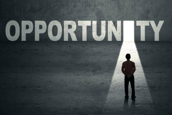 A businessman standing in front of a door with the term opportunity mentioned in front of him.