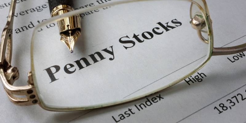 Image of a newspaper magnifying the term penny stocks, through a spectacle and a pen kept near it.