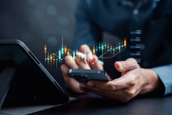 A person using a tab and a calculator with virtual images of trading data and graph.