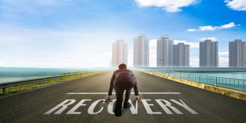 A businessman on the road ready to run toward the city on Recovery.