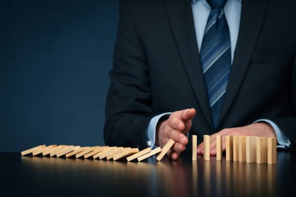 An investor stopping the domino effect of falling wooden blocks depicting risk management.