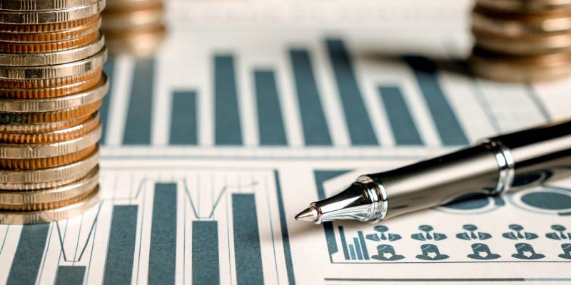 A Pile of coins stack kept on charts along with a pen indicating treasury management.